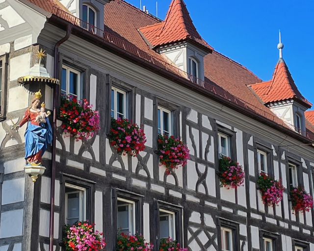 Amtsgebäude der Stadt Forchheim in der Sattlertorstraße Ein Fachwerkgebäude mit Blumenschmuck an den Fenstern und mit Dacherkern und einer Marienfigur an der Hausecke.