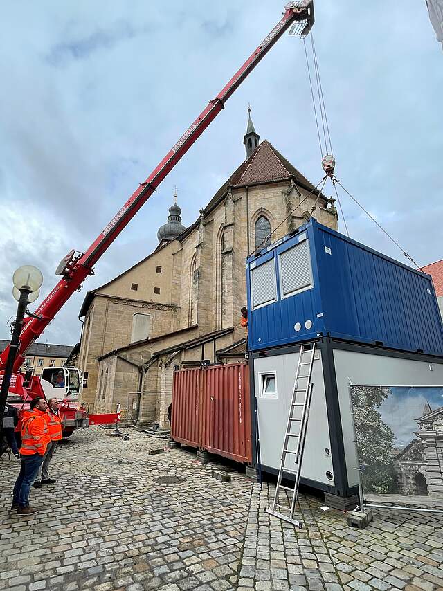 Ein Kran stapelt große Baucontainer übereinander.