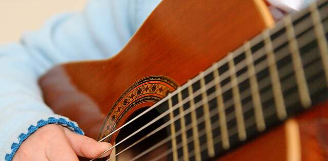 Ausschnitt einer Gitarre, an der ein Kind musiziert.