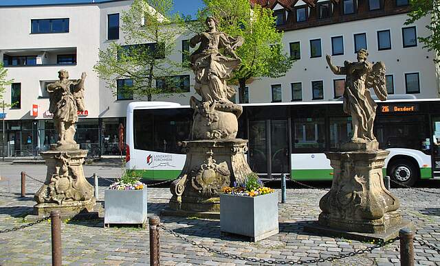 Mariengruppe am Paradeplatz in Forchheim. Drei Figuren auf einem Platz, im Hintergrund ist ein Omnibus und eine Häuserfassade zu sehen.