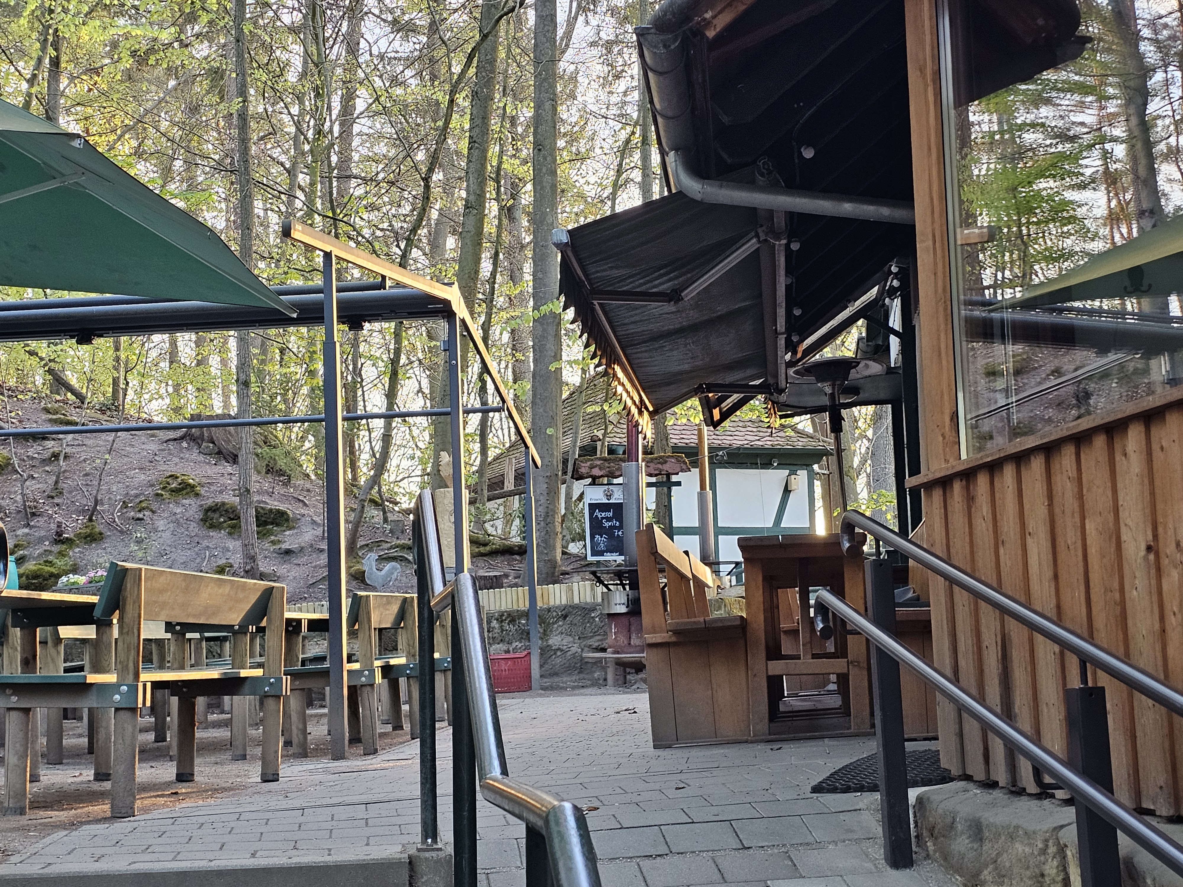 Glockenkeller Aufgang mit Blick auf mehrere Biergarnituren, Schonnenschutz und dem Anbau des Glockenkellers im Forchheimer Kellerwald