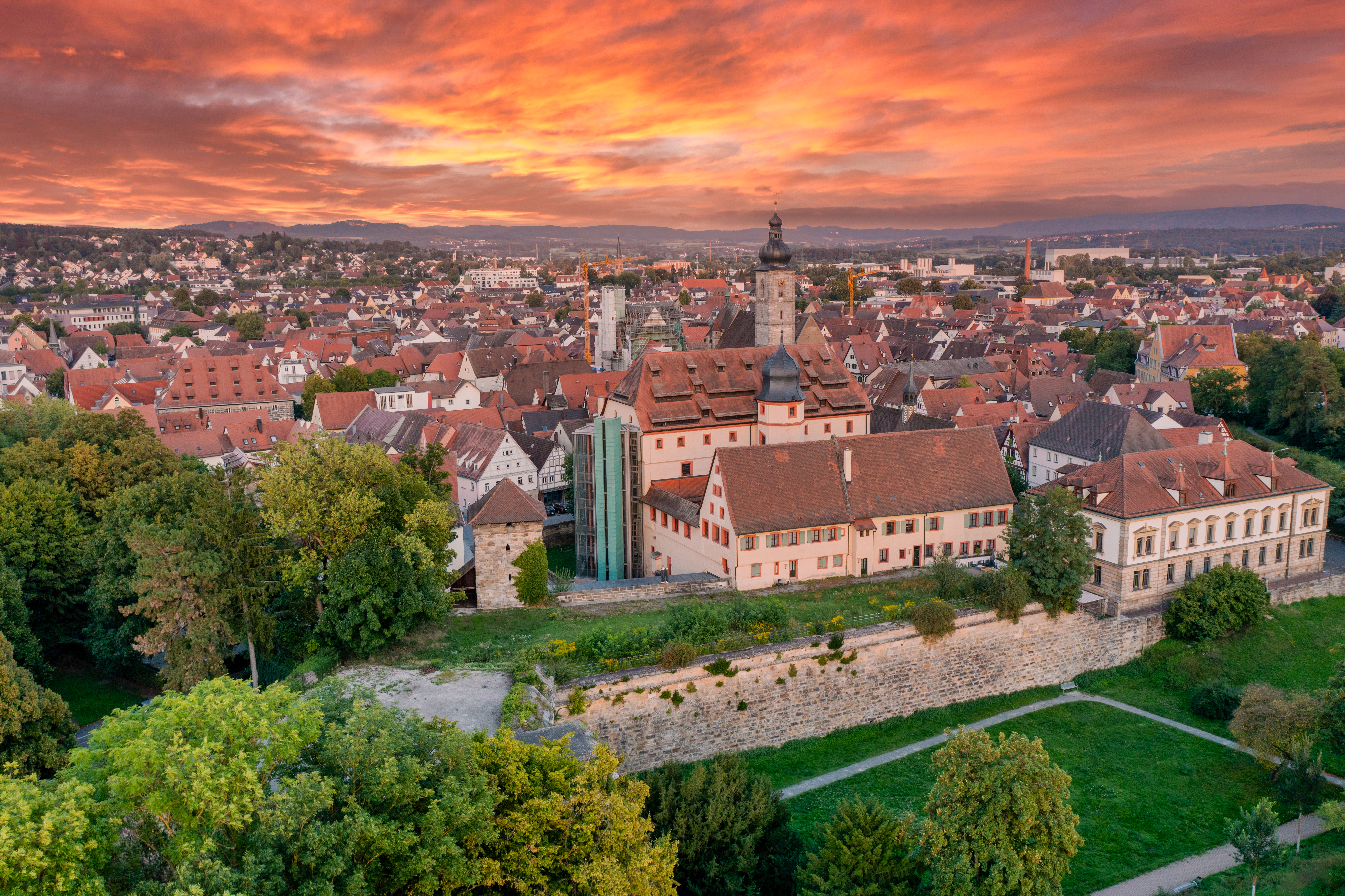 Luftbildaufnahme der Stadt Forchheim bei Sonnenaufgang. Im Hintergrund die Beginn der Fränkischen Schweiz mit den Bergen "Walberla" und "Rodenstein".