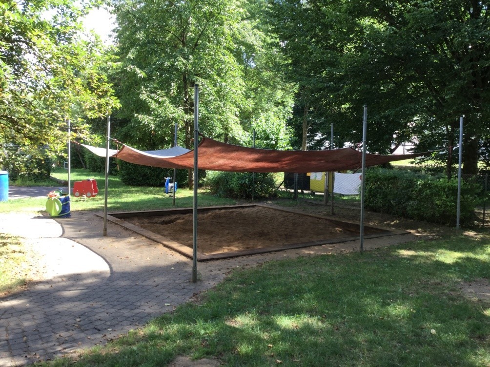 Außenbereich mit Spielgeräten Außenspielbereich mit überdachtem Sandkasten und Schaukeltieren.